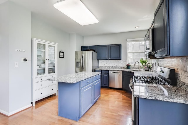 kitchen featuring decorative backsplash, blue cabinets, appliances with stainless steel finishes, a center island, and a sink