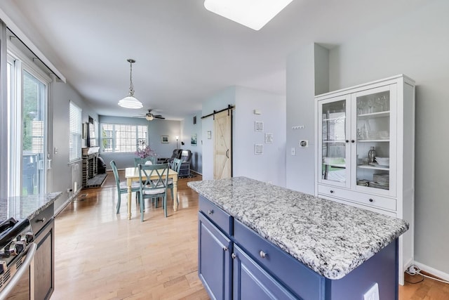 kitchen with open floor plan, light wood-type flooring, a barn door, gas stove, and blue cabinetry