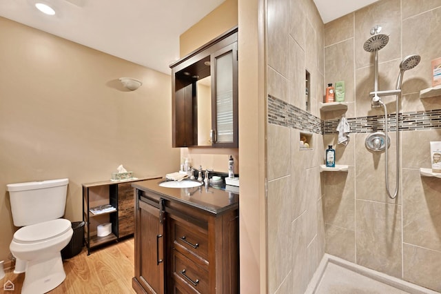 bathroom featuring tiled shower, toilet, wood finished floors, and vanity
