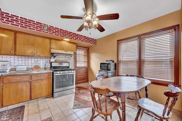 kitchen featuring under cabinet range hood, stainless steel range with gas cooktop, ceiling fan, tasteful backsplash, and light countertops