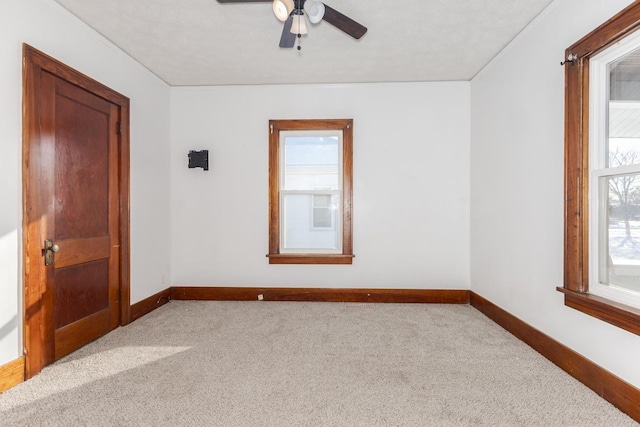 carpeted spare room featuring baseboards and a ceiling fan