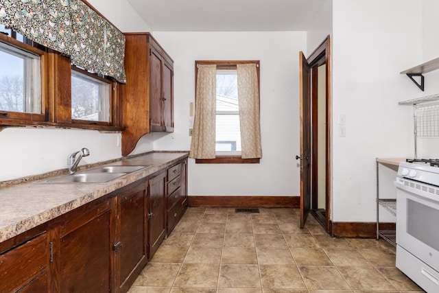 kitchen featuring baseboards, a sink, visible vents, and gas range gas stove