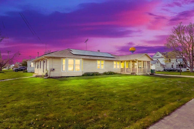 view of front of house featuring roof mounted solar panels, covered porch, and a front yard