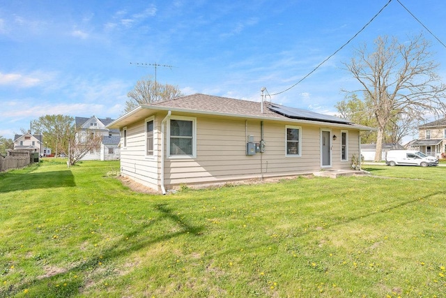 rear view of house featuring roof mounted solar panels and a yard
