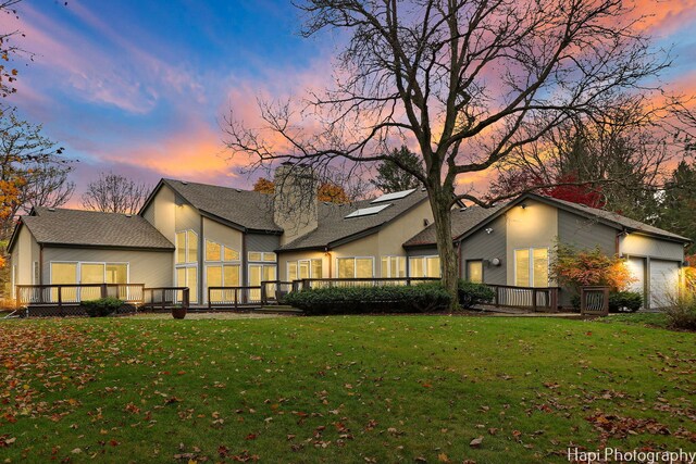 back of property at dusk with a yard, a chimney, a deck, and a garage