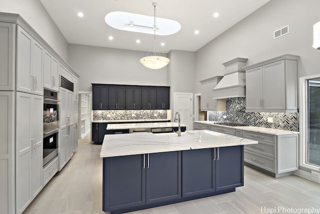 kitchen with tasteful backsplash, a sink, a center island with sink, a high ceiling, and visible vents