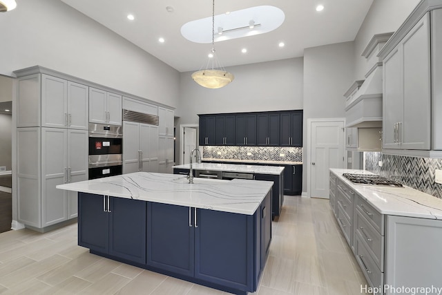 kitchen featuring a sink, decorative backsplash, a kitchen island with sink, a towering ceiling, and appliances with stainless steel finishes