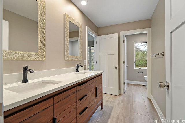 full bathroom featuring double vanity, baseboards, a sink, and toilet