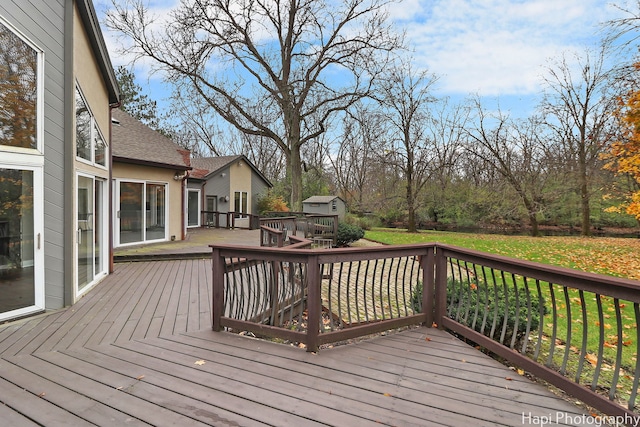 wooden terrace featuring a lawn, a storage unit, and an outbuilding