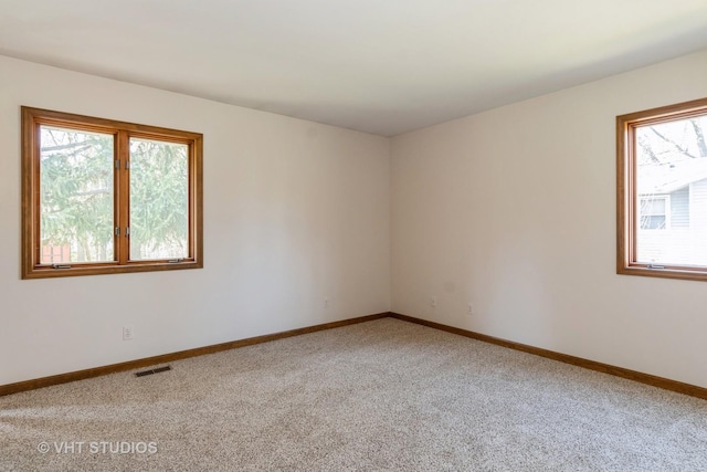 spare room featuring light colored carpet, visible vents, and baseboards