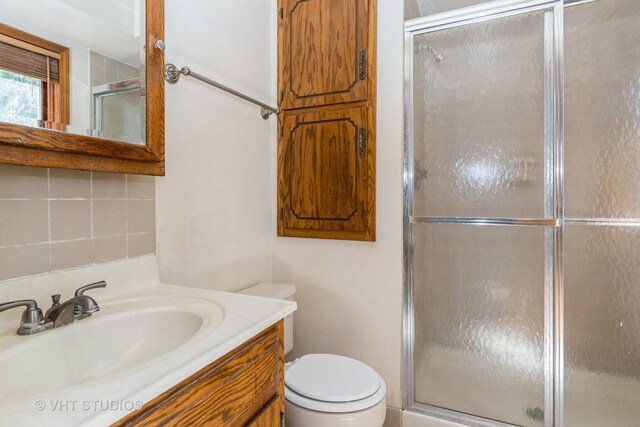 full bathroom featuring toilet, a stall shower, vanity, and tasteful backsplash