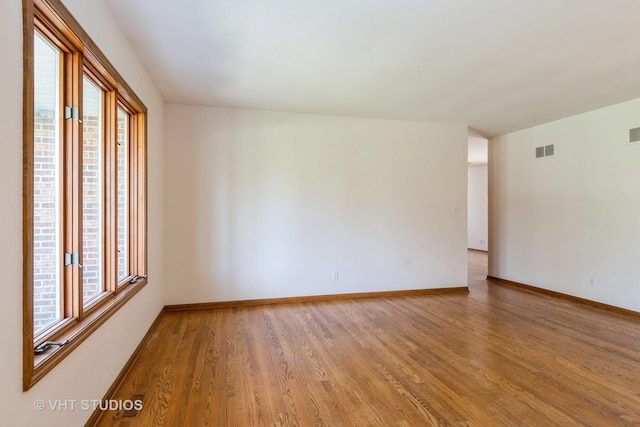 empty room with baseboards, visible vents, light wood finished floors, and plenty of natural light