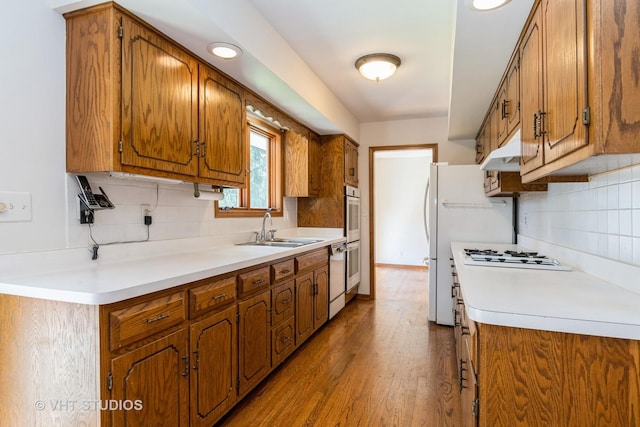 kitchen with brown cabinetry, wood finished floors, white appliances, and a sink