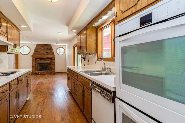 kitchen with a sink, a brick fireplace, white appliances, dark wood-type flooring, and light countertops