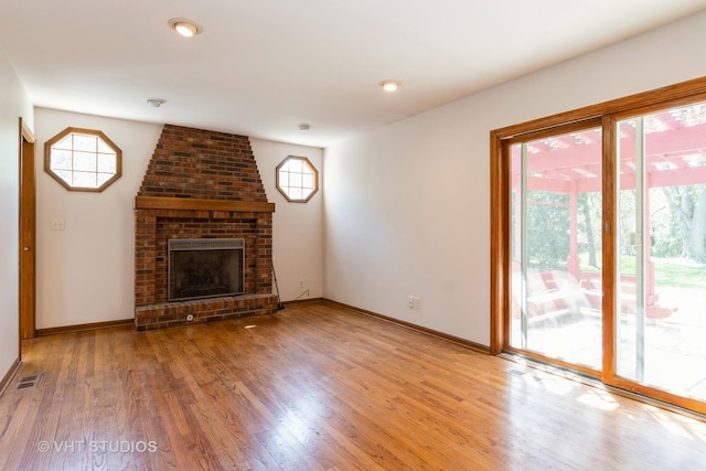 unfurnished living room with baseboards, visible vents, light wood-type flooring, and a brick fireplace