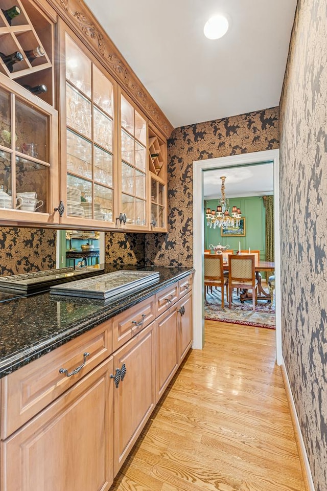 1135 Buttonwood Ln, Northbrook, IL 60062 - kitchen featuring light wood-style flooring, wallpapered walls, glass insert cabinets, a chandelier, and dark stone countertops