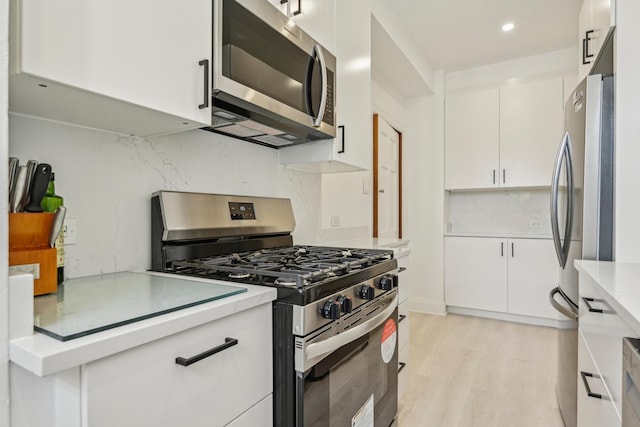 kitchen featuring stainless steel appliances, white cabinets, light countertops, light wood-style floors, and decorative backsplash