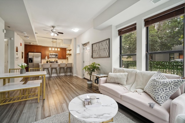 living area with baseboards, a ceiling fan, light wood finished floors, and visible vents