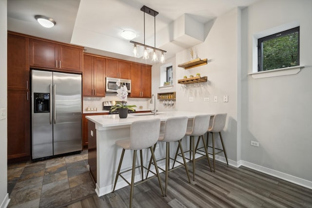 kitchen with a peninsula, a breakfast bar, light countertops, appliances with stainless steel finishes, and backsplash