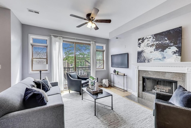 living area with visible vents, wood finished floors, a fireplace, baseboards, and ceiling fan