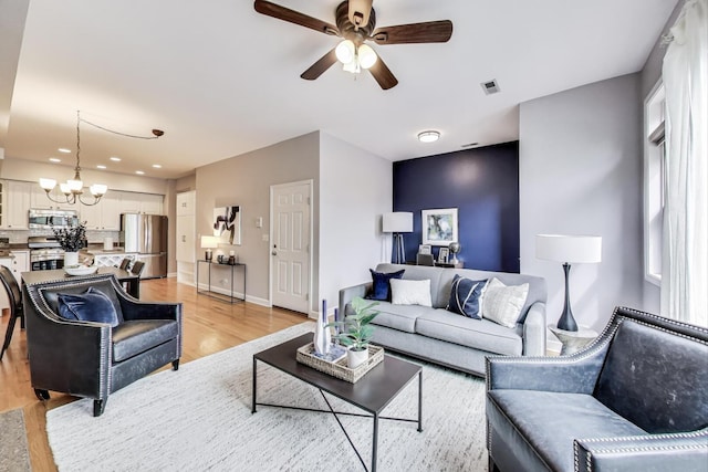 living room with visible vents, light wood-style floors, baseboards, recessed lighting, and ceiling fan with notable chandelier