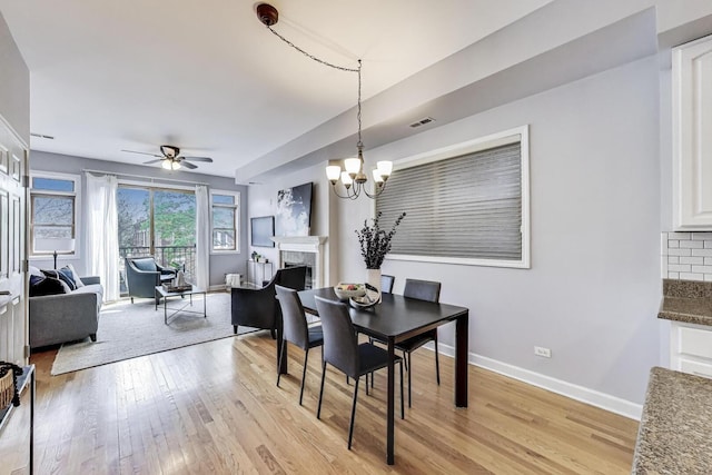dining area with baseboards, light wood finished floors, visible vents, and a fireplace