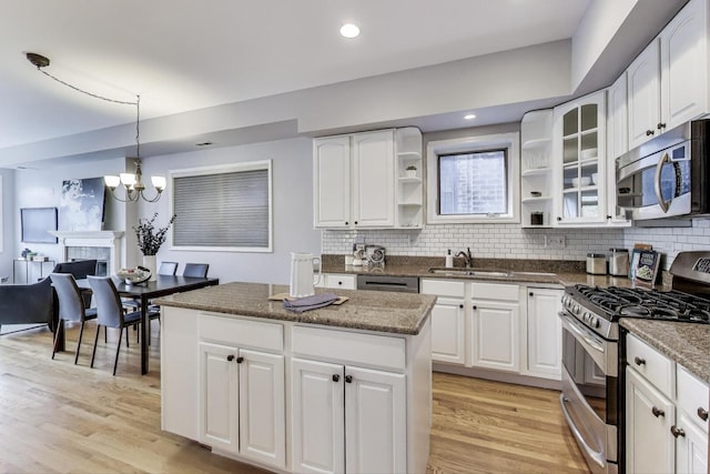 kitchen featuring decorative backsplash, appliances with stainless steel finishes, open shelves, a sink, and light wood finished floors