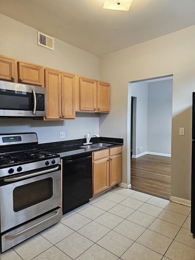 kitchen featuring stainless steel appliances, a sink, dark countertops, visible vents, and light tile patterned floors