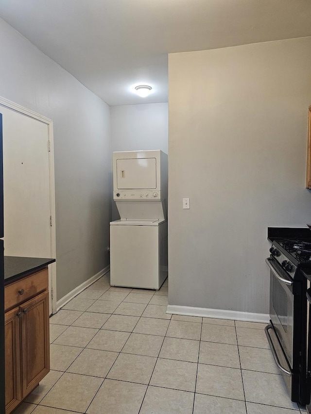 interior space featuring baseboards, light tile patterned flooring, stacked washer and dryer, and laundry area