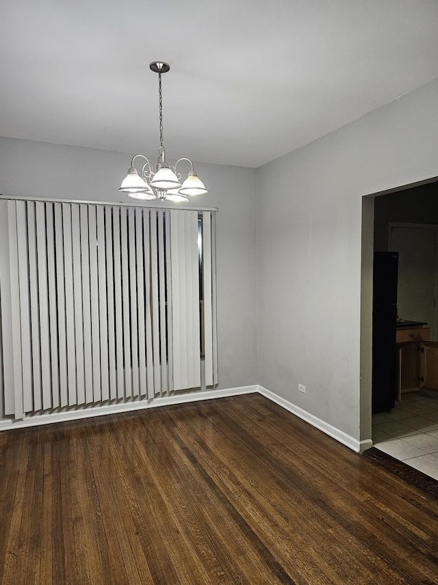 spare room with wood finished floors, baseboards, and an inviting chandelier