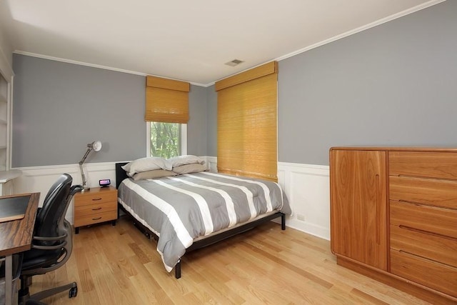 bedroom featuring light wood-style floors, visible vents, crown molding, and a wainscoted wall