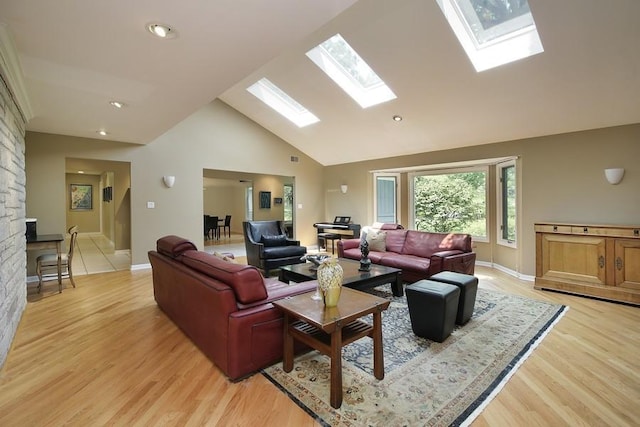 living area with a skylight, baseboards, high vaulted ceiling, and light wood finished floors