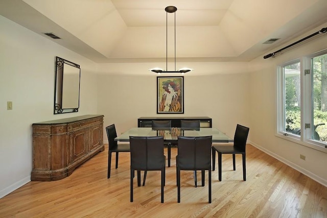 dining area with light wood finished floors, baseboards, visible vents, and a raised ceiling