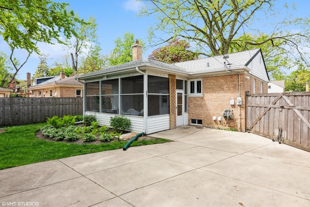 rear view of property featuring a sunroom, a chimney, brick siding, fence, and a gate
