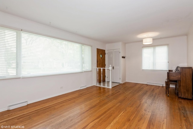 unfurnished living room featuring baseboard heating, light wood finished floors, a baseboard radiator, and baseboards