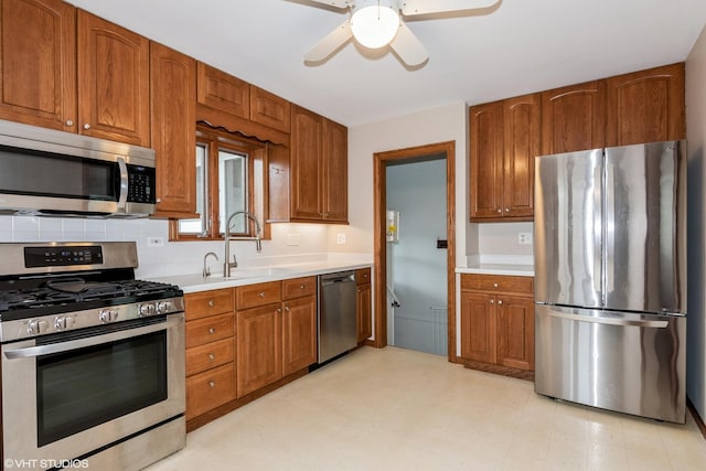 kitchen with appliances with stainless steel finishes, a sink, light countertops, and brown cabinetry
