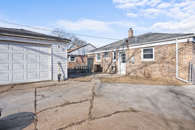 exterior space with a chimney, concrete driveway, a garage, brick siding, and a patio area