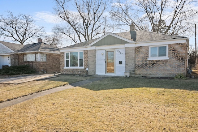 view of front of property featuring brick siding, a front yard, a shingled roof, and a chimney