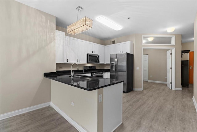 kitchen featuring a peninsula, appliances with stainless steel finishes, a sink, and light wood-style flooring