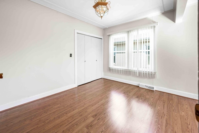 unfurnished bedroom featuring wood finished floors, visible vents, crown molding, and baseboards