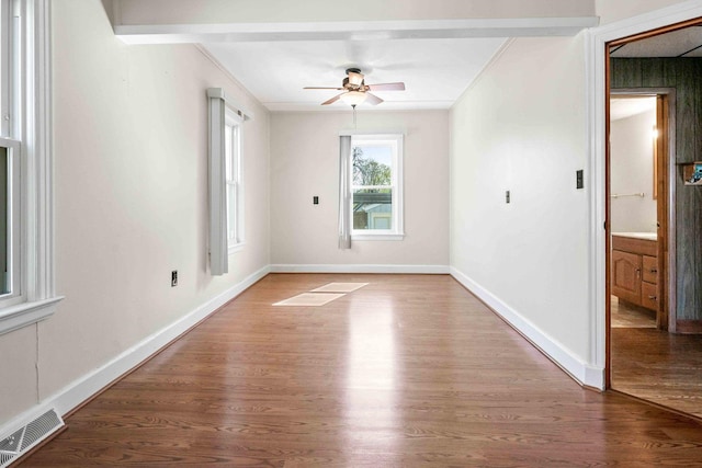 empty room with wood finished floors, visible vents, a ceiling fan, and crown molding