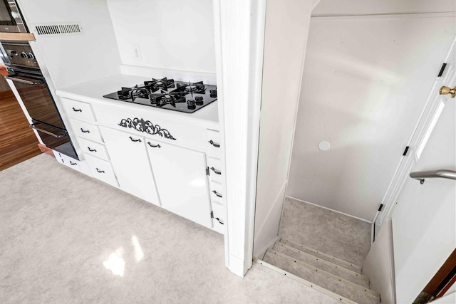 interior space with white cabinets, light countertops, arched walkways, black appliances, and light colored carpet