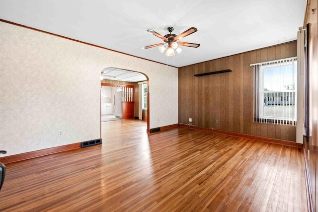spare room with arched walkways, wood finished floors, visible vents, and ceiling fan
