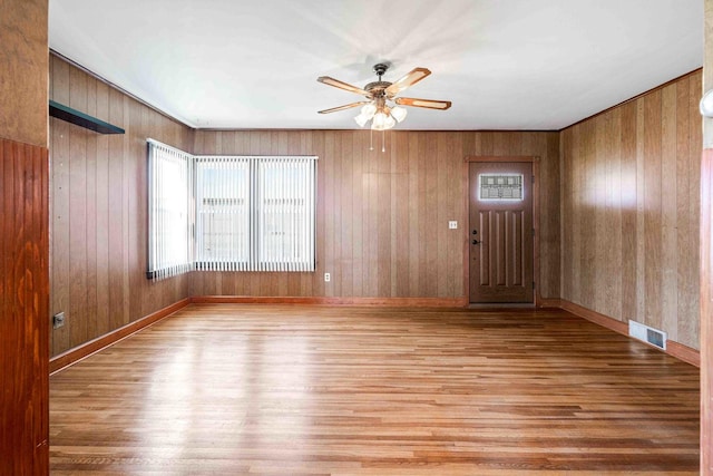 empty room with wood finished floors, visible vents, wood walls, and ceiling fan
