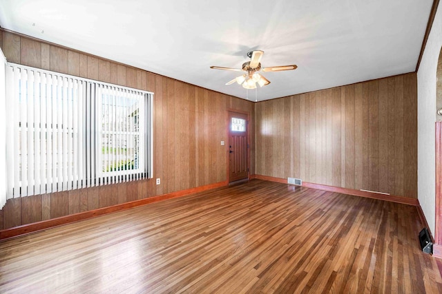 spare room featuring a ceiling fan, wood walls, wood finished floors, baseboards, and visible vents