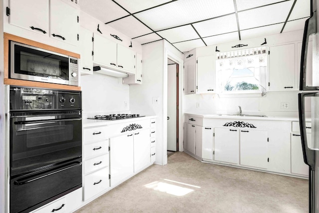 kitchen with white cabinets, stainless steel microwave, a warming drawer, light countertops, and black oven