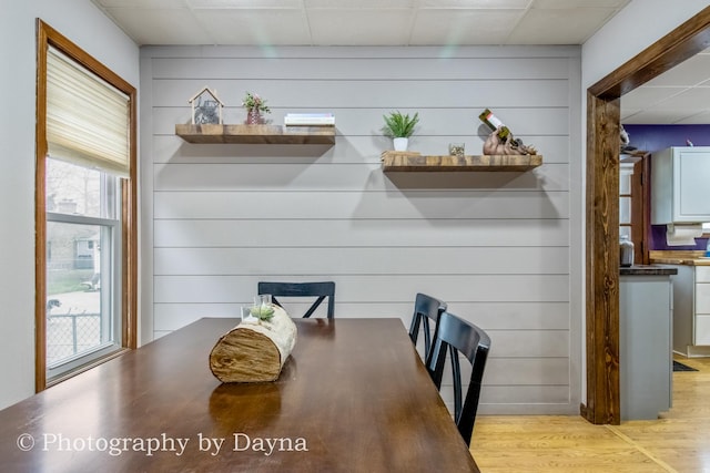 dining room featuring light wood-style flooring, wooden walls, and a drop ceiling