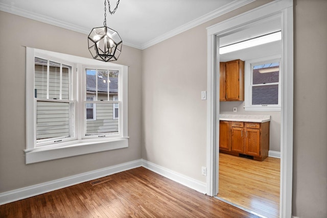 unfurnished dining area with light wood-type flooring, an inviting chandelier, baseboards, ornamental molding, and visible vents