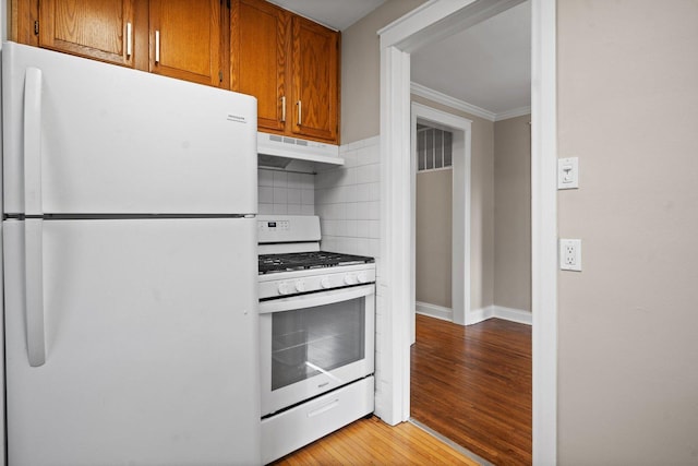 kitchen featuring under cabinet range hood, ornamental molding, brown cabinetry, white appliances, and light wood-style flooring