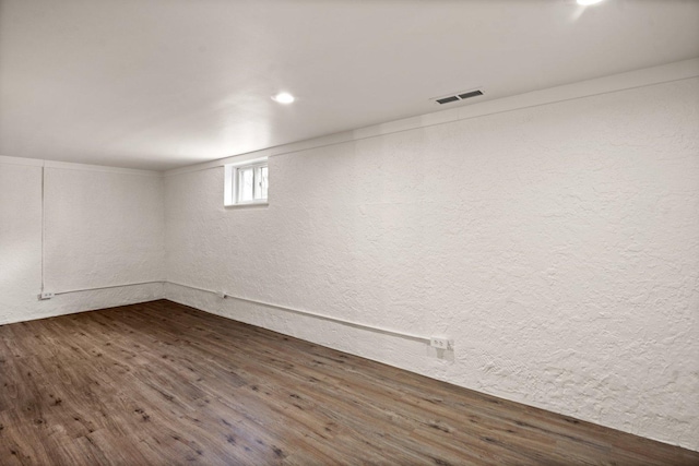 below grade area featuring dark wood finished floors, a textured wall, and visible vents
